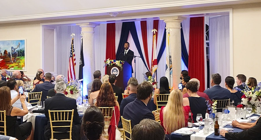 Speaker addressing seated guests during a formal corporate gala at The Club at Iron Lake in Ocala, Florida.