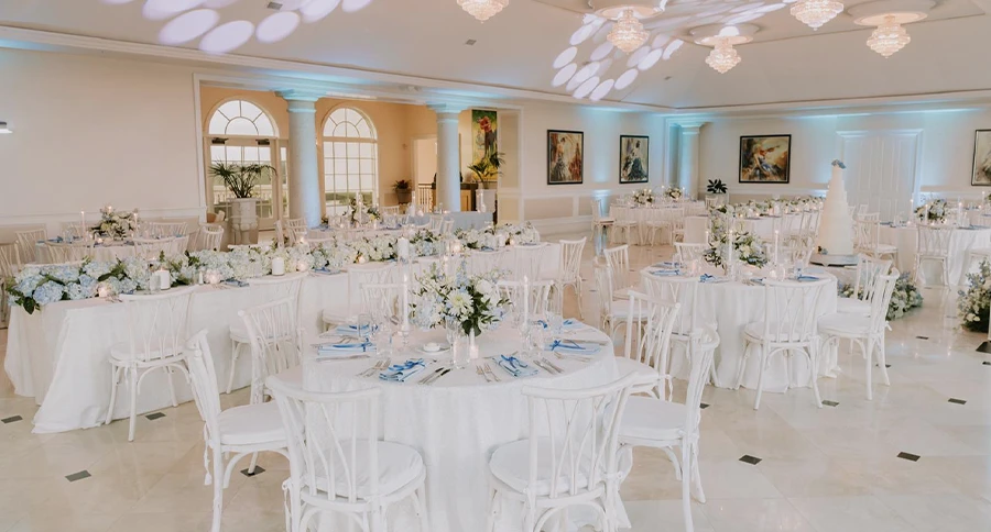 Elegant wedding reception ballroom at The Club at Iron Lake with white tables, floral arrangements, chandeliers, and a wedding cake.